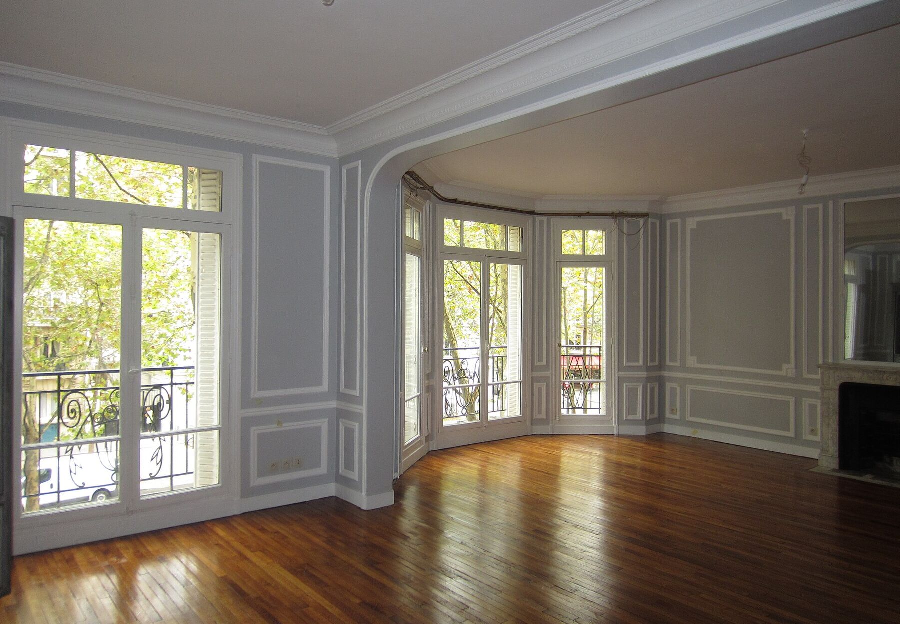 Séjour vide d'un appartement ancien lumineux, avec moulures, parquet ciré, cheminée en marbre et portes-fenêtres à balcon